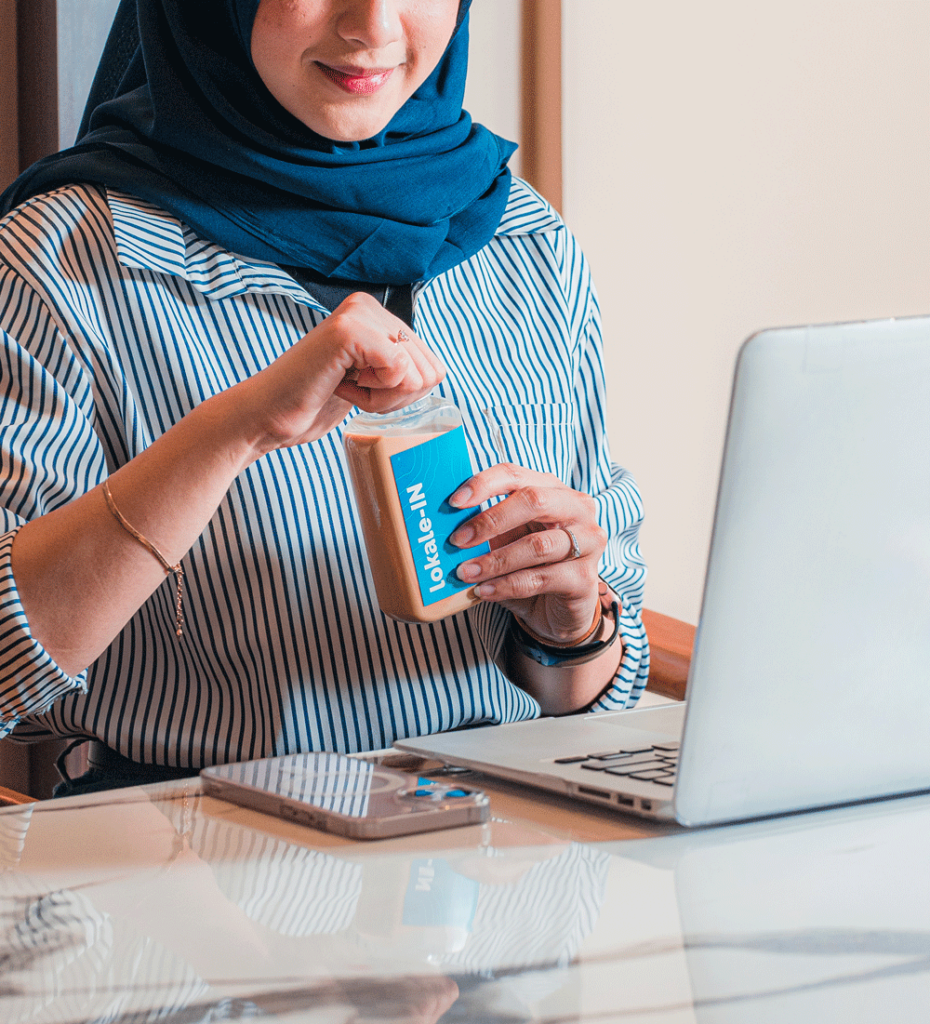 seorang perempuan muda sedang membuka botol lokaleIN yakni salah satu produk dari lokale coffee, didepan laptop